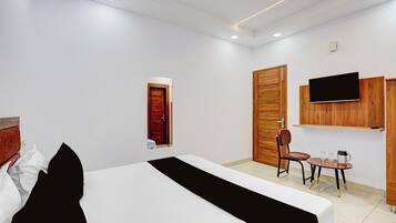 A hotel room with a bed, a desk with a chair, a television mounted on the wall, and a wooden wardrobe.