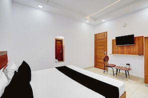 Habitación de hotel con cama, escritorio con silla, televisión instalada en la pared y armario de madera.
