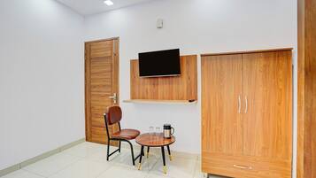 Una habitación con un armario de madera, un televisor montado en la pared, una silla y una pequeña mesa con un hervidor.
