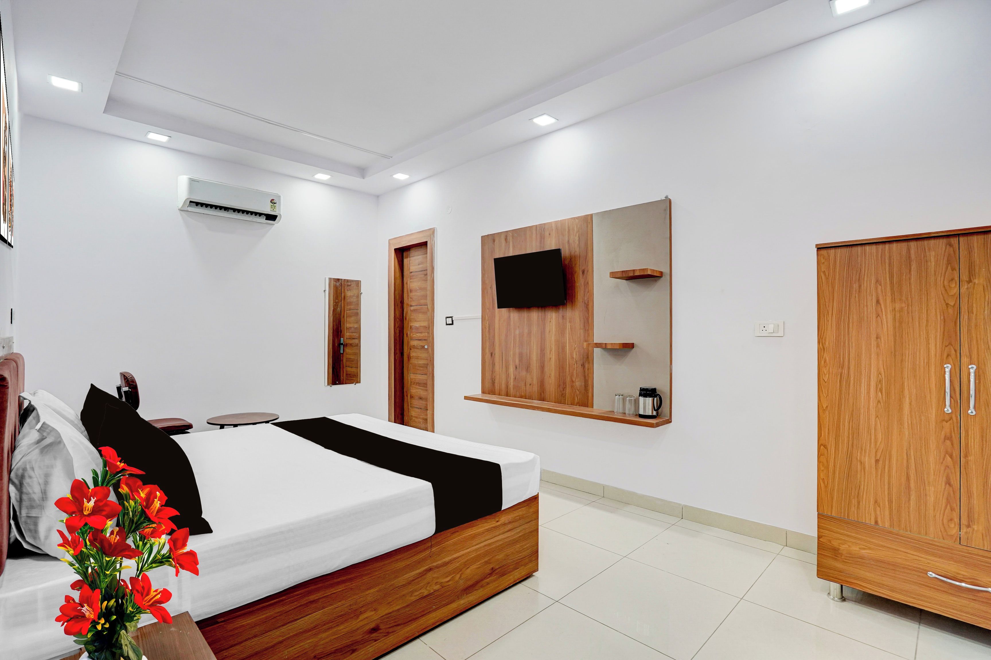 A modern bedroom with a bed, wooden wardrobe, a mounted TV, and an air conditioning unit.