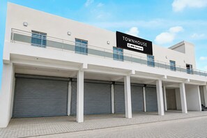 A modern townhouse with a large sign advertising Oyo-Serviced. It features a flat facade, multiple garage doors, and a balcony with metal railings.