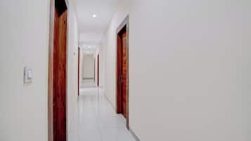 A corridor with white tiled flooring, wooden doors, and recessed ceiling lighting.