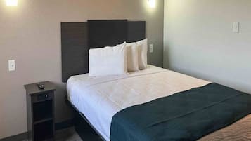 A hotel room with a bed, a nightstand, and a wall-mounted light fixture.