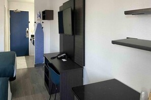 A hotel room with a desk, chair, television, and a small table.