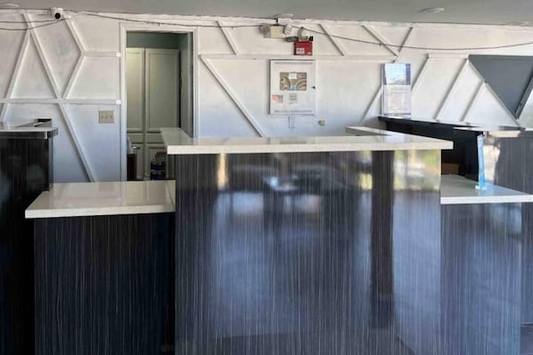 A reception desk with a modern design, a fire alarm, and a door leading to another room.