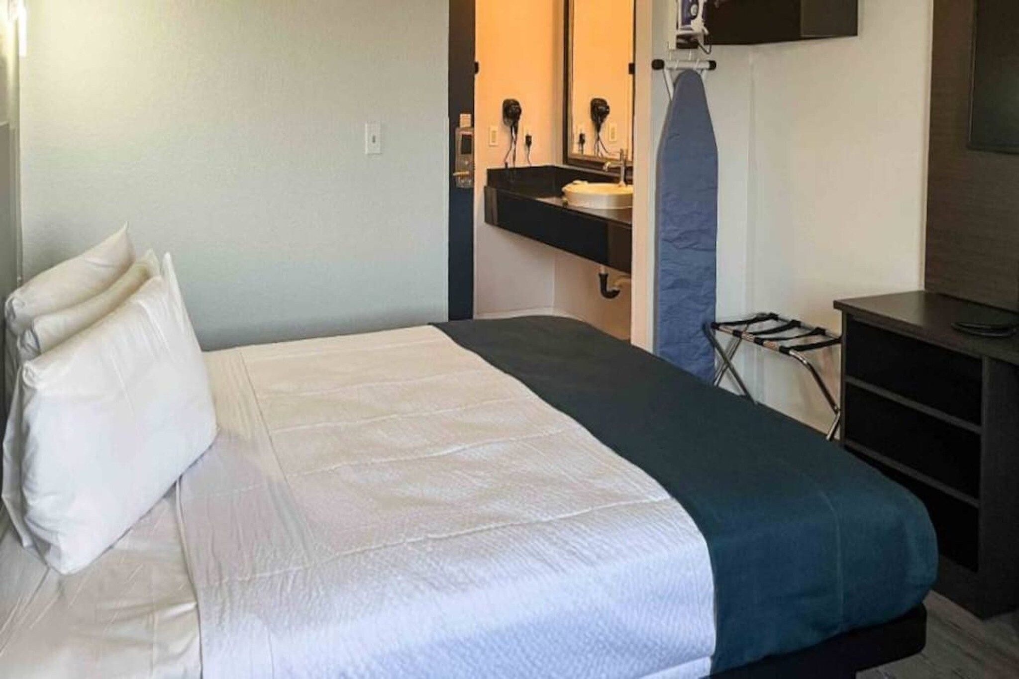 A hotel room with a bed, a desk, a chair, a mirror, and a hairdryer.