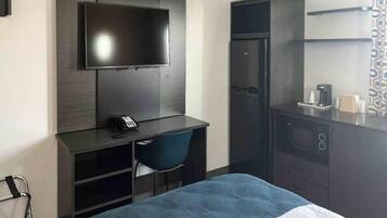 Habitación de hotel compacta con una cama, un escritorio con silla, televisor, refrigerador y microondas.