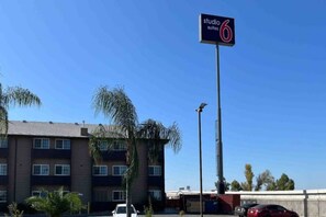Hotelschild mit der Aufschrift Studio Suites 6, im Hintergrund ein mehrstöckiges Gebäude und Palmenbäume.