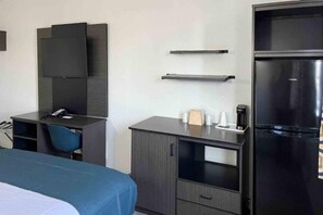 A hotel room with a bed, a desk, a chair, a flat-screen TV, a refrigerator, and a coffee maker.