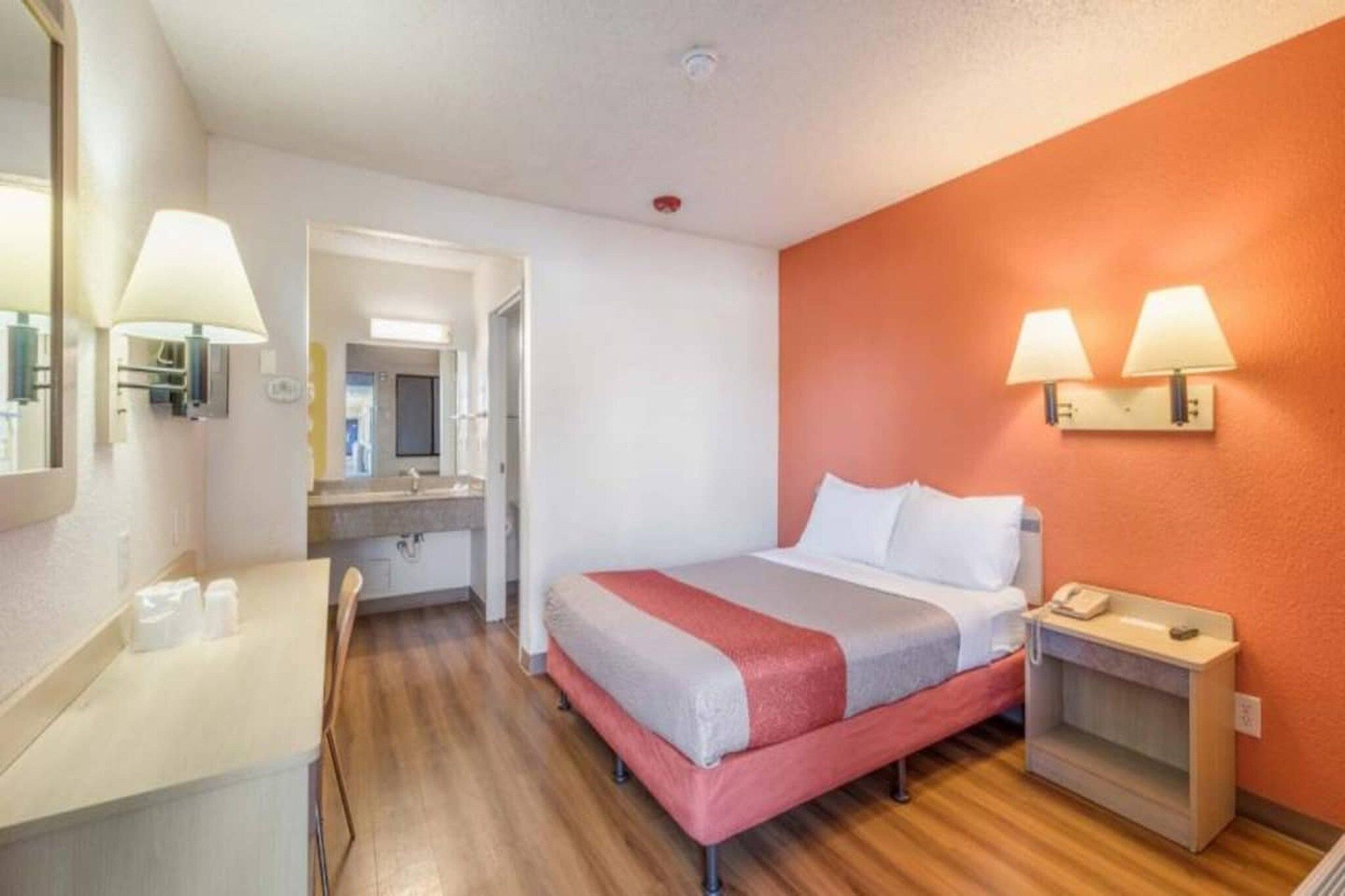 Habitació d'hotel amb llit, taula de nit, làmpada i mirall.