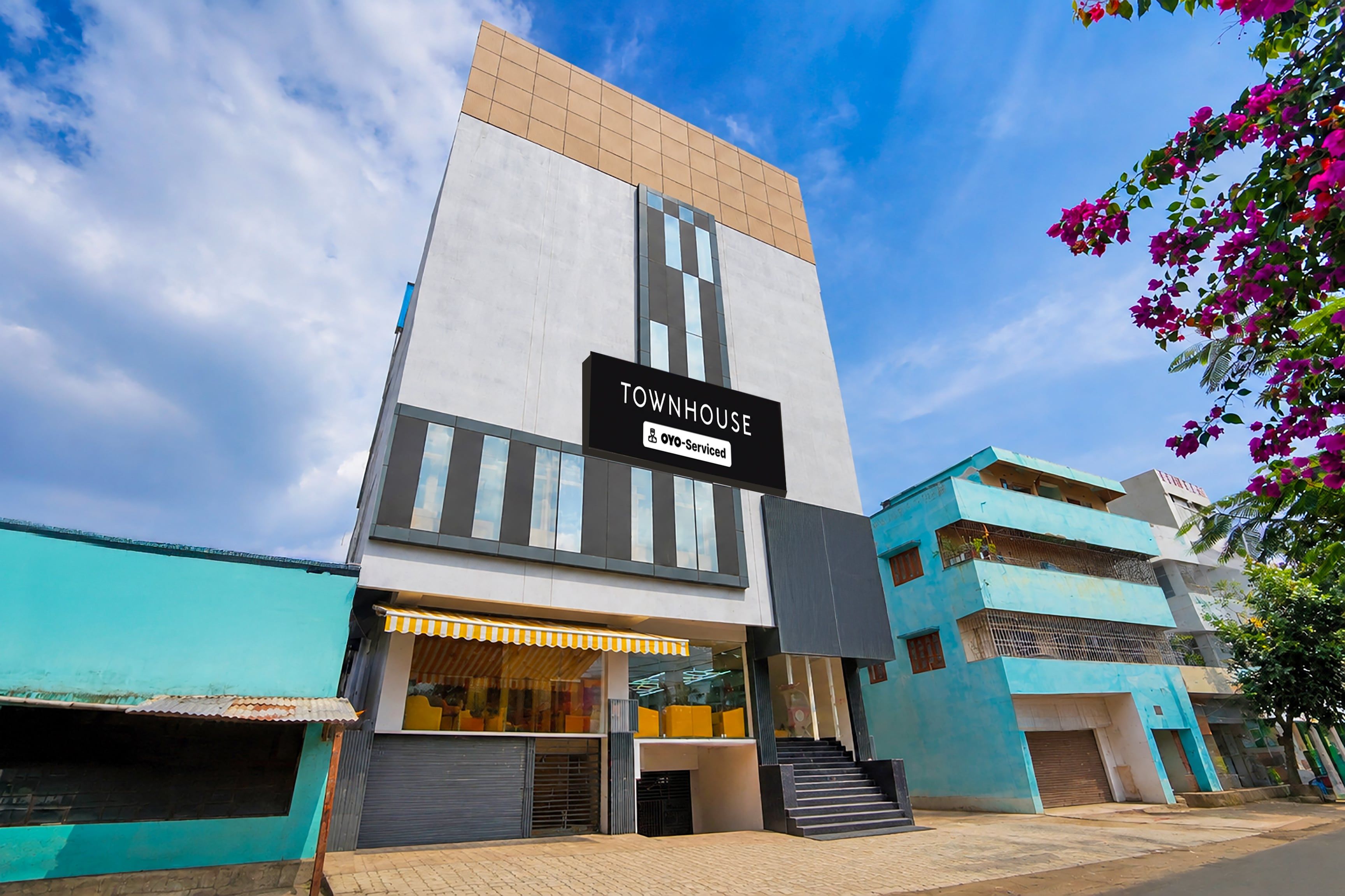 A modern townhouse with a prominent 'TOWNHOUSE' sign, a covered entrance, and a staircase leading to the entrance.