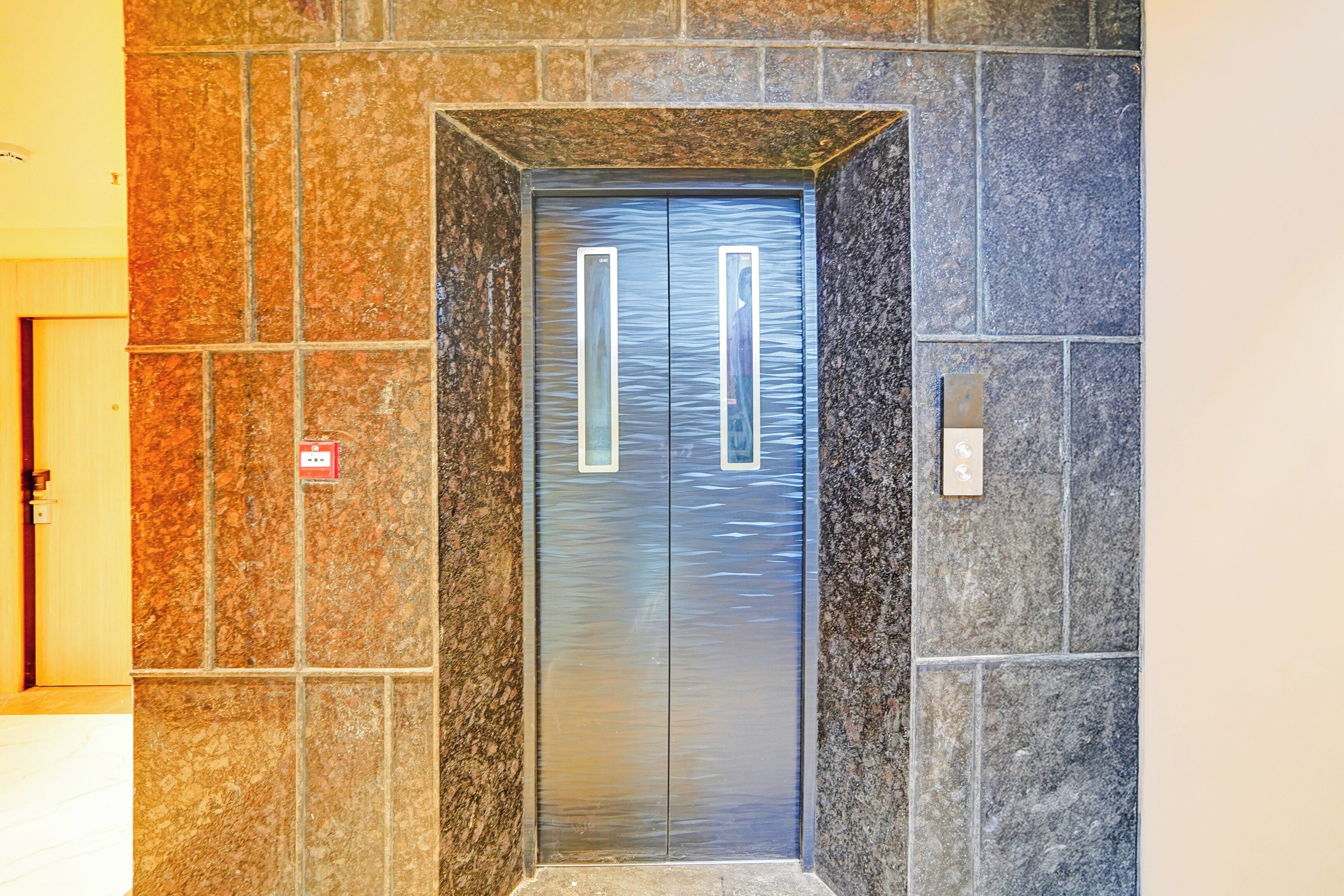 A modern elevator with a metallic finish, set within a stone wall.