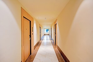 A hotel corridor with wooden doors, a marble floor, and a view into a room at the end. - Townhouse Patna Airport (Patna)