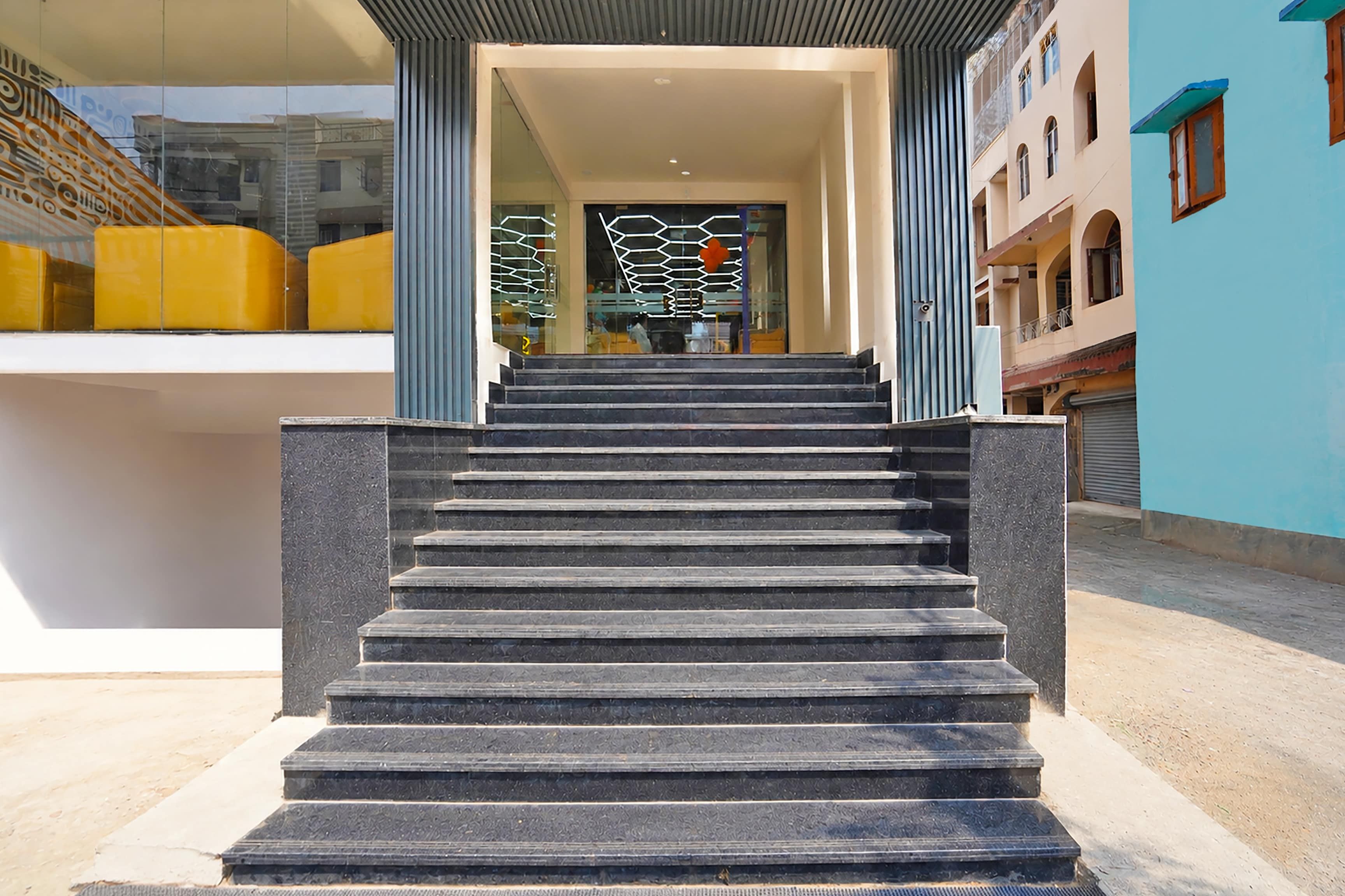 Una escalera conduce a la entrada de un edificio con puerta de vidrio y una valla metálica decorativa.