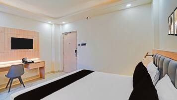 A hotel room with a bed, a desk, a chair, a television, and a door.