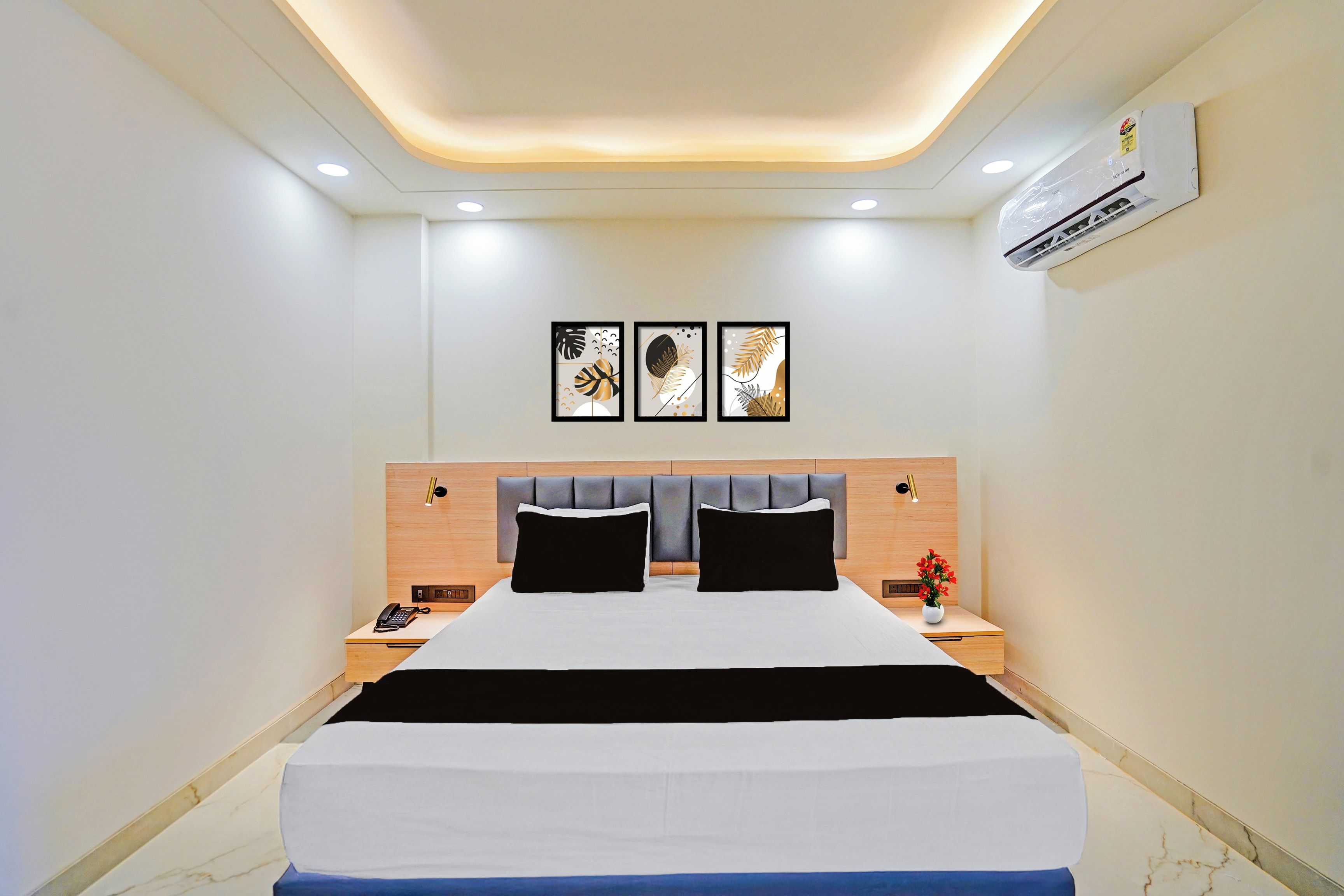 Una habitación de hotel con cama, mesitas de noche, teléfono, aire acondicionado y decoración en la pared.