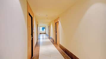 A hotel corridor with doors on both sides, a marble floor, and a view of a window at the end.