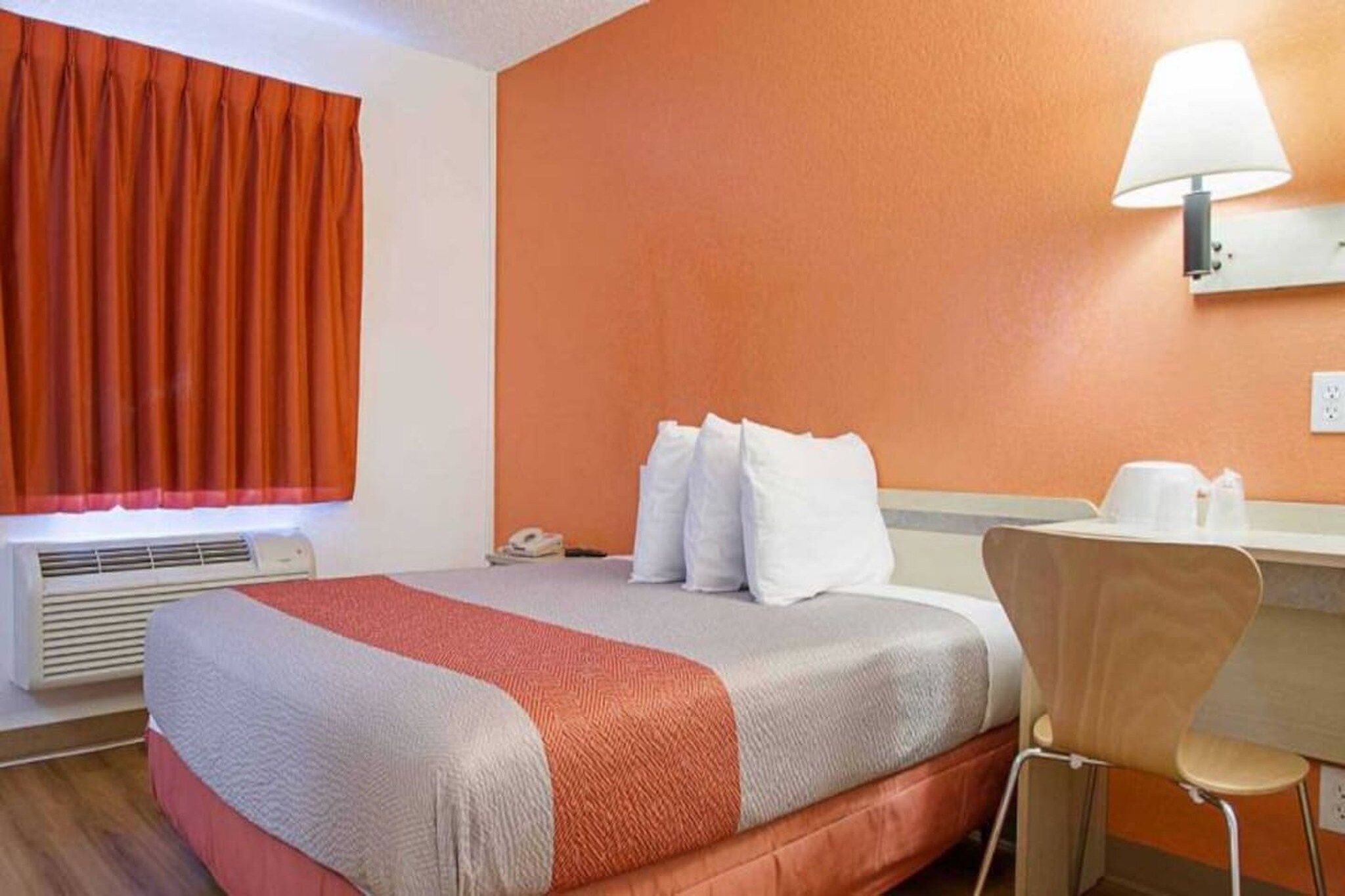 Een hotelkamer met een bed, een bureau, een stoel, een lamp en een raam met gordijnen.