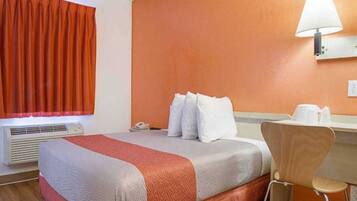 Een hotelkamer met een bed, een bureau, een stoel, een lamp en een raam met gordijnen.