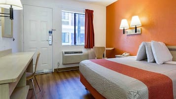 A hotel room with a bed, bedside table, desk, chair, window with curtains, and wall-mounted lamps.
