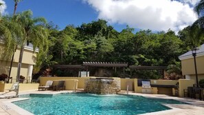 Ein Pool mit Wasserfall, umgeben von Liegestühlen und einer Pergola.