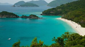 Eine Küstenlandschaft mit Strand, klarem türkisblauem Wasser und üppigen grünen Hügeln.
