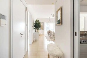 A hallway with a white bench, a potted plant, and a dining area in the background. - ELEGANT 1 Bed with Marina View - Marian Tower - Dubai Marina (Dubai)