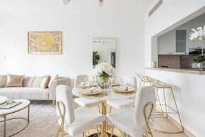 Een moderne woonkamer met een bank, eettafel en stoelen. Er is een keuken met kasten en een aanrecht.