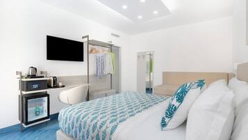 A hotel room with a bed, a desk with a coffee machine, a wardrobe, and a TV mounted on the wall.
