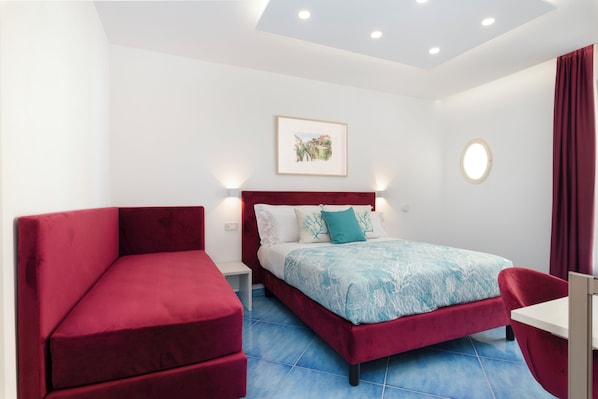 A modern bedroom with a bed, a red sofa, a small table, and a wall-mounted picture. - Cornelia Rooms (Sorrento)