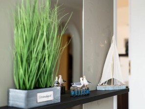 Ein Regal mit einer Blumentopf-Pflanze, zwei Seemannsfiguren, einem 'WELCOME'-Schild und einem Modellboot.