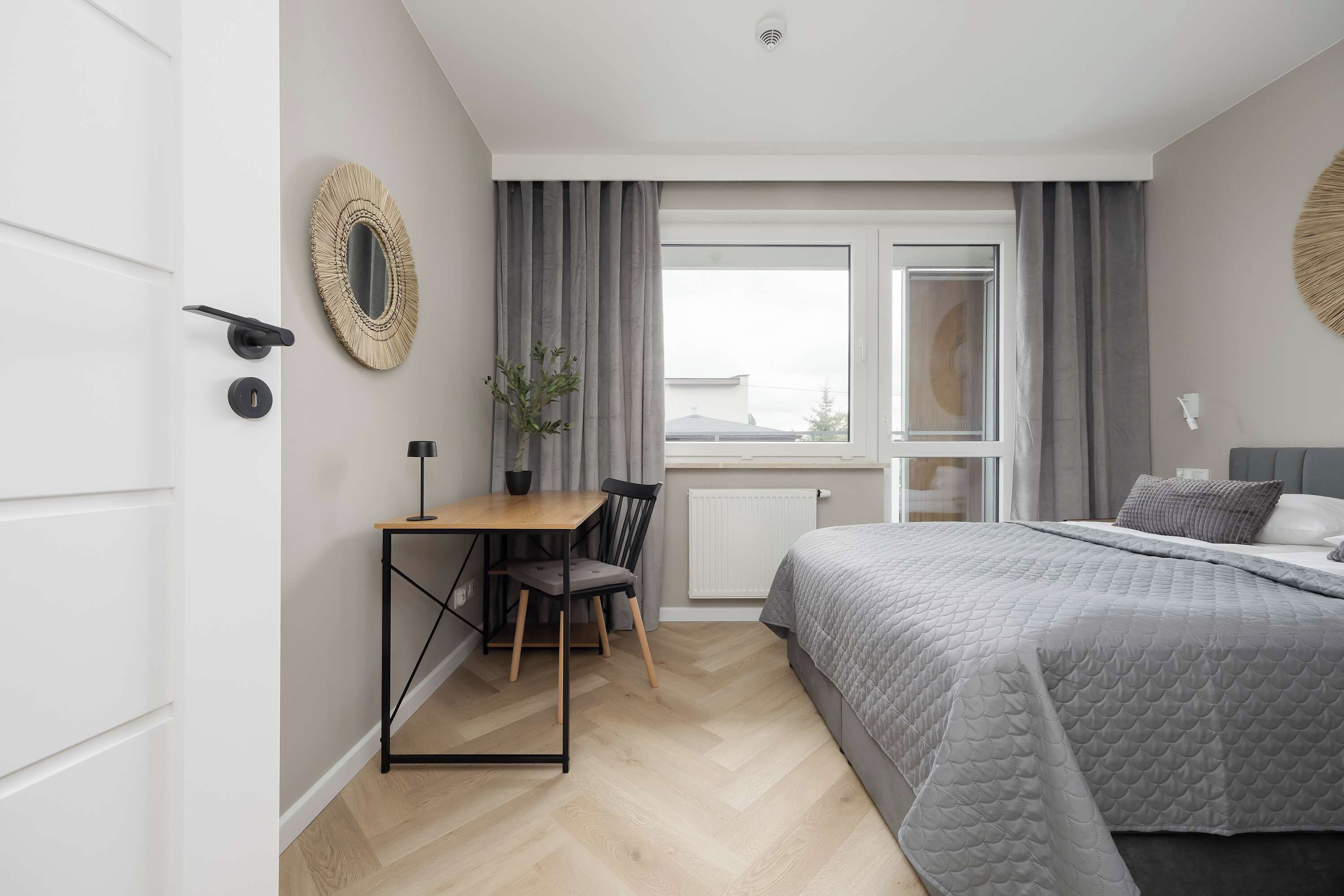 A bedroom with a bed, a desk, a chair, a radiator, and a window with curtains.