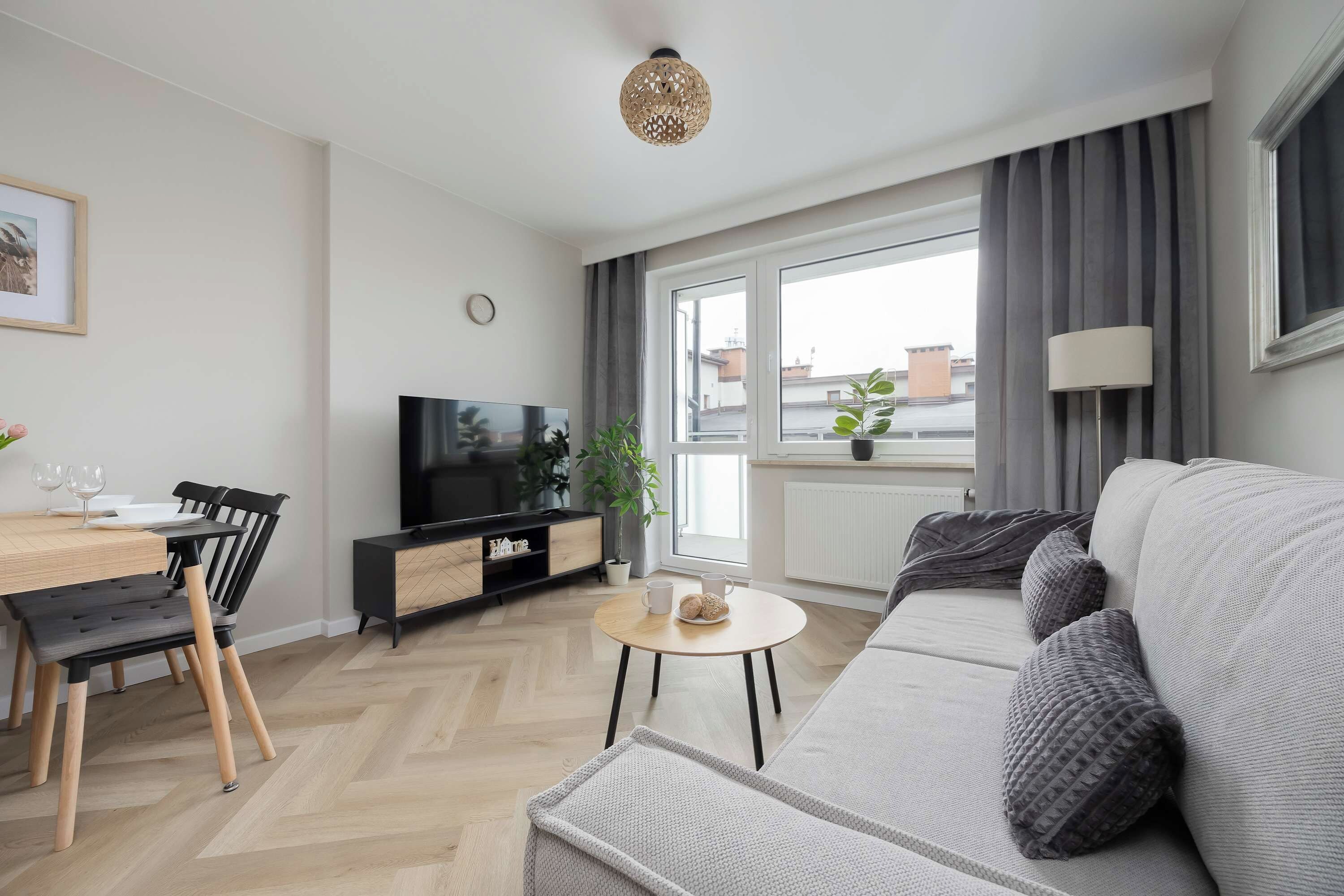 Un salon moderne comprenant un canapé, une table à manger avec des chaises, un téléviseur et une fenêtre avec des rideaux.