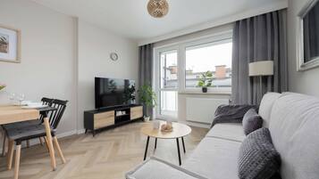 Un salon moderne comprenant un canapé, une table à manger avec des chaises, un téléviseur et une fenêtre avec des rideaux.