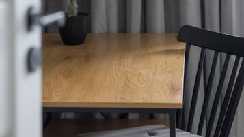 A wooden dining table with a potted plant, a black chair with a cushioned seat, and a curtain in the background.