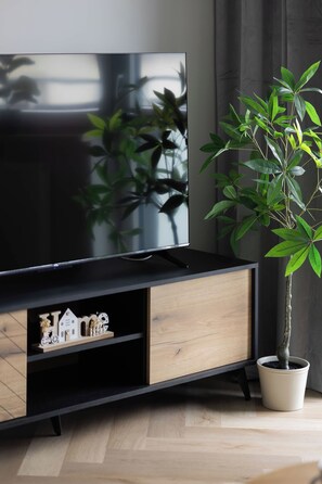 Un téléviseur à écran plat, posé sur un pied noir, avec un meuble en bois en dessous.