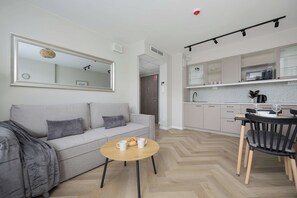 Un espace de vie moderne comprenant un canapé, une petite table ronde et un coin cuisine avec des placards et un plan de travail.