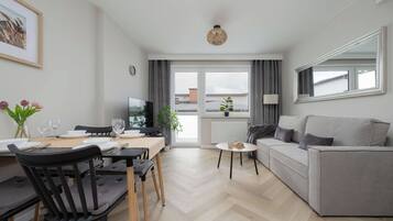 A modern living room with a sofa, dining table, chairs, and a television.
