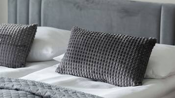 A neatly made bed with a grey headboard and pillows, a grey quilted blanket, and a textured throw.