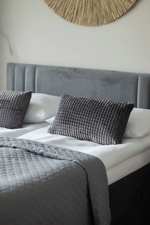 Ein ordentlich bezogenes Bett mit grauem Kopfteil und Kissen, einer gesteppten grauen Decke und einer strukturierten Tagesdecke.