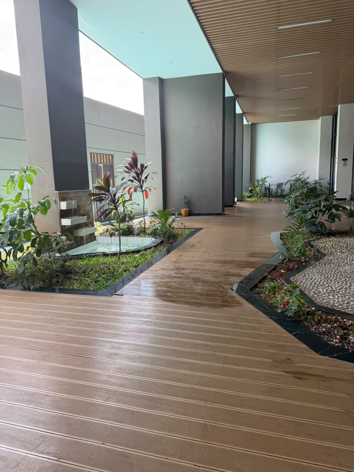 A modern indoor corridor with a wooden floor, surrounded by planters with various plants and flowers.