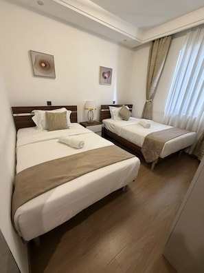 Una habitación de hotel con dos camas, una mesita de noche con lámpara y una ventana con cortinas.