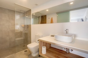 A modern bathroom with a glass-enclosed shower, a white toilet, and a large sink with a mirror above. - Cozy studio apartment in the Kikere Complex (Puerto del Carmen)