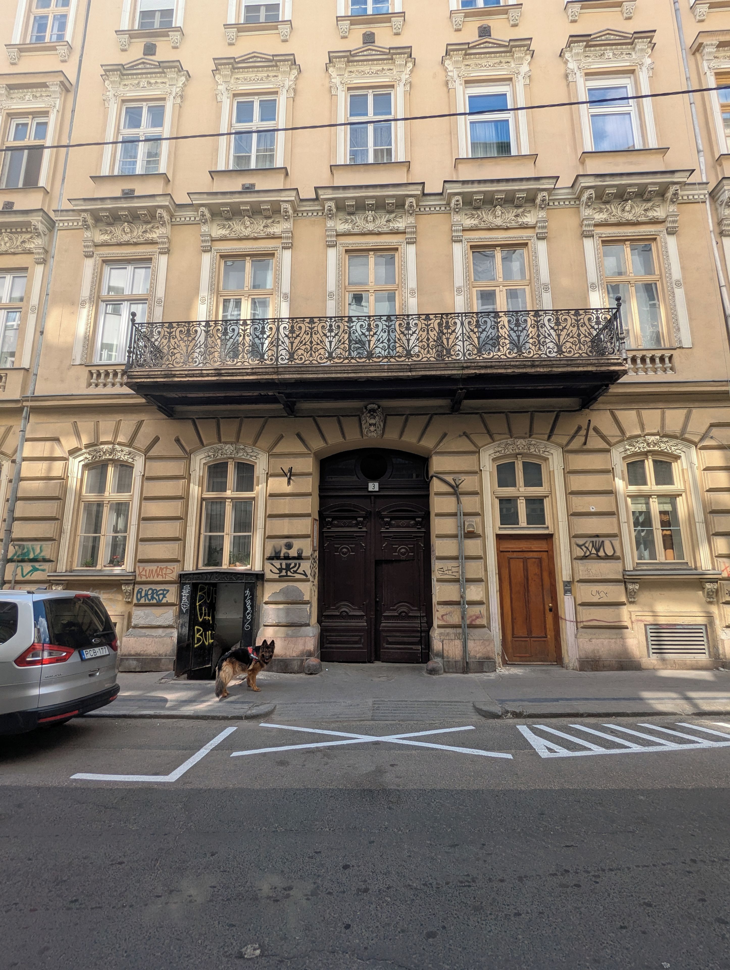 A building with a large entrance, ornate balconies, and a dog in front.