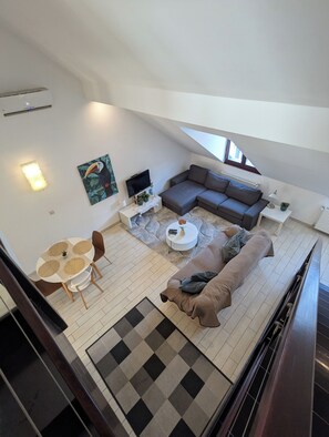 A modern loft-style living space with a sectional sofa, a dining table with chairs, a small round coffee table, and a flat-screen TV mounted on the wall. - Astoria Panorama Duplex, Self-check-in, Automated, Large, 2lvl apt with a view (Budapest)