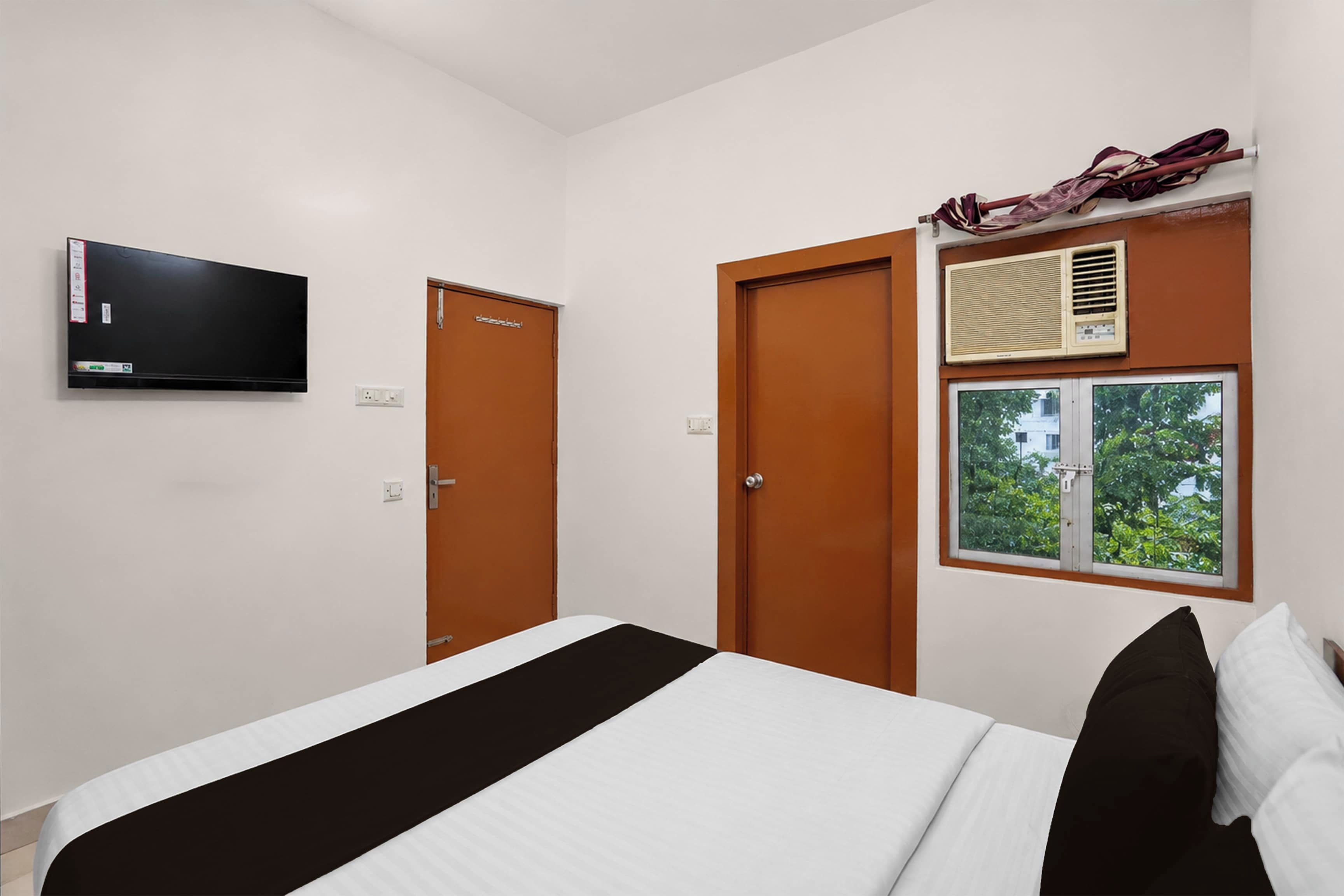 Habitación de hotel con cama, televisor, dos puertas y ventana con unidad de aire acondicionado encima.