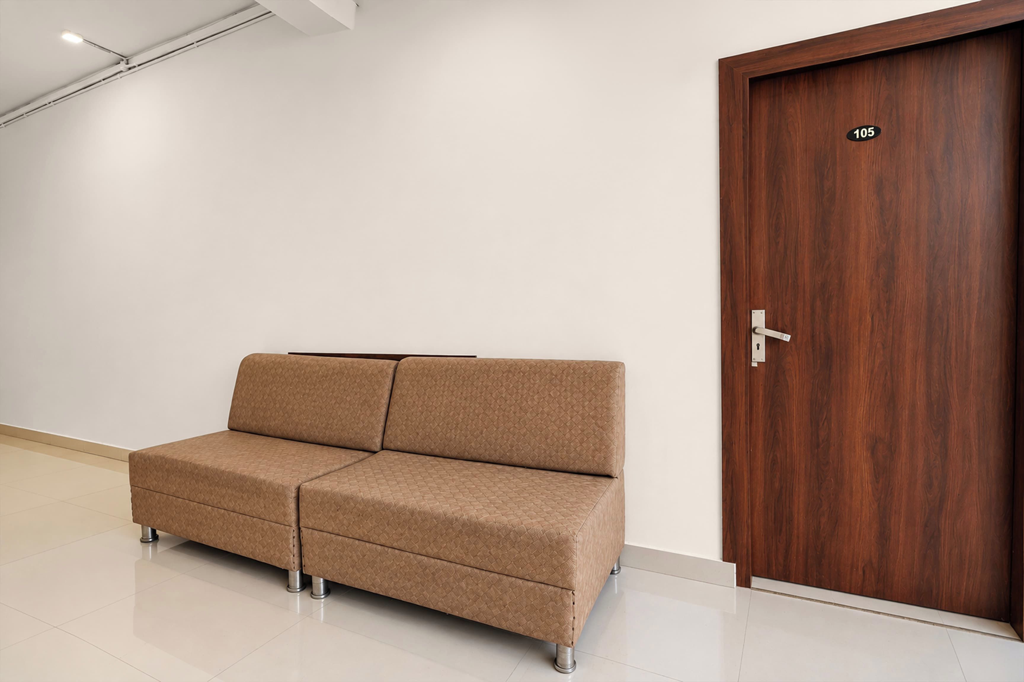 Una habitación con un sofá marrón, una puerta de madera con un número y una pared blanca.