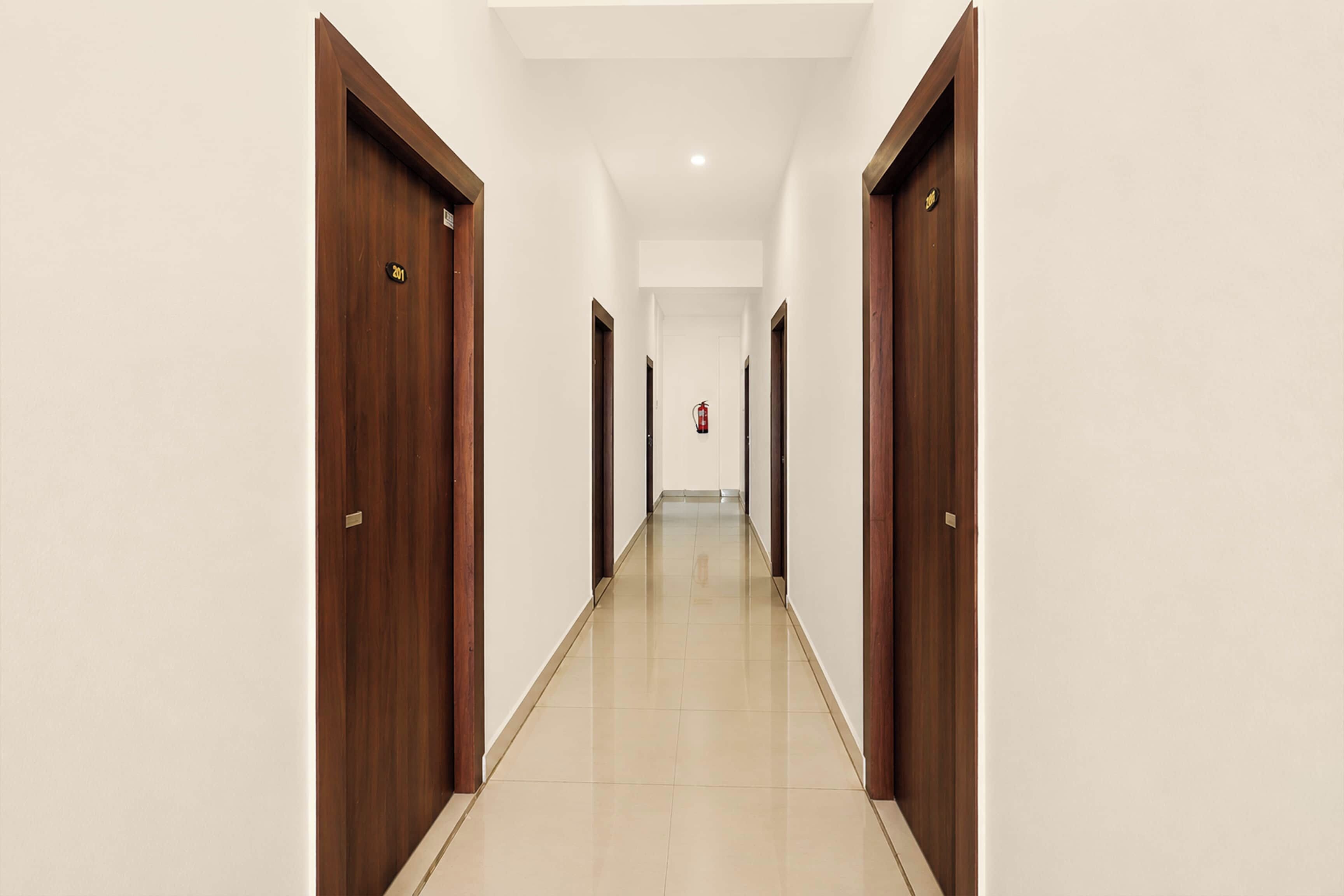 Corredor com portas de madeira, um extintor de incêndio e piso de azulejos limpo.
