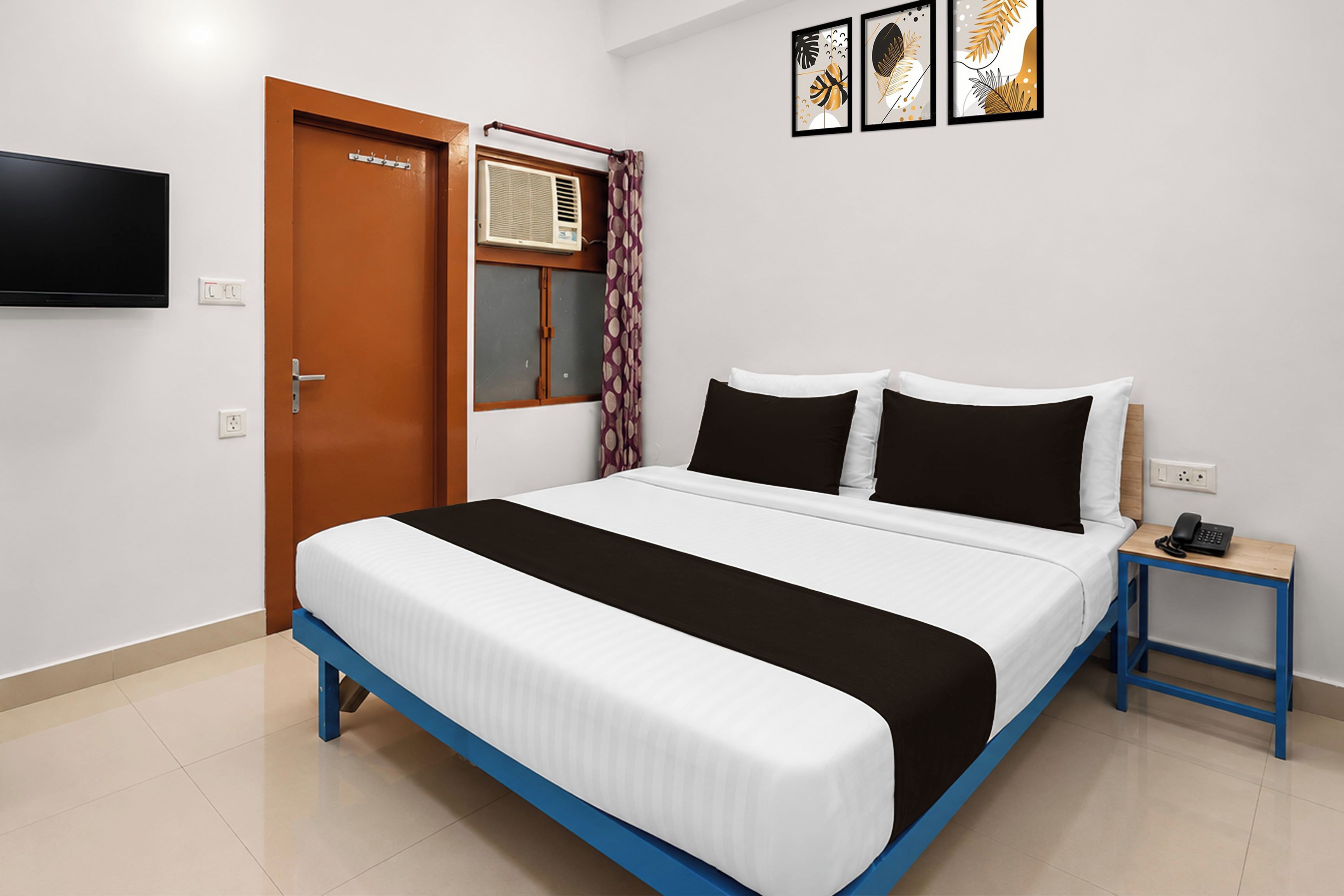 Habitación de hotel con cama, mesita de noche con teléfono, televisor montado en la pared y puerta con manija.