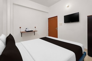 Een hotelkamer met een bed, een aan de muur bevestigde televisie, een deur en een plankje met een waterkoker en bekers.